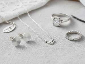 A close-up shot of various sterling silver jewelry pieces including a delicate necklace, a pair of stud earrings, and a ring, gleaming against a soft, neutral background, highlighting their quality and versatility.