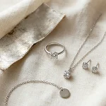 Custom silver jewelry flat lay collection of sterling silver ring pendant necklace stud earrings and bracelet on cream linen