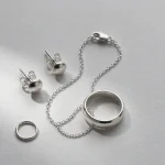 Flat lay of nickel-free 925 sterling silver jewelry collection including stud earrings necklace clasp ring and jump ring on gray surface